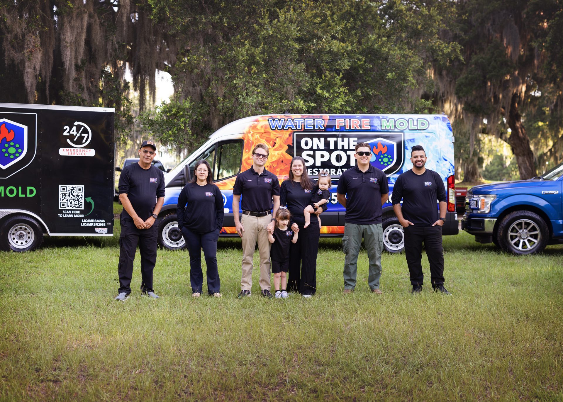 A team of six individuals poses outdoors in front of vehicles branded for mold services, set against a natural backdrop.