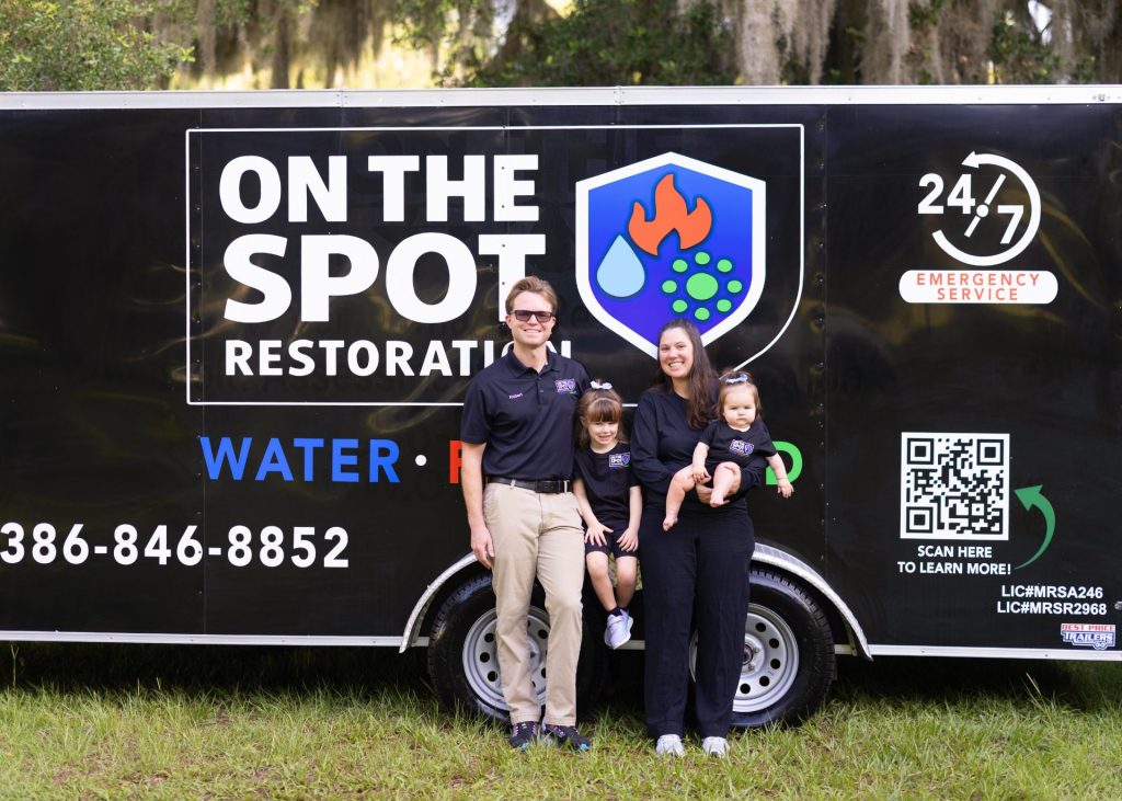 A family poses in front of a trailer with the words 'On The Spot Restoration', promoting their water damage restoration services.