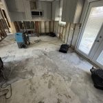 A partially stripped interior space with exposed wall studs, a concrete floor, and several fans for drying.