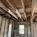 Interior of a building under renovation, featuring exposed wooden beams, concrete walls, and Windows with natural light.