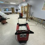 A spacious room with partial walls, a red machine in the foreground, and various cleaning equipment scattered around.