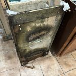 A damaged refrigerator with mold and deterioration, positioned on tiled flooring among other kitchen items.