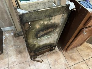 A damaged refrigerator with mold and deterioration, positioned on tiled flooring among other kitchen items.
