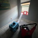 A blue device appears near a window with a red structure, alongside a red cart on a bare floor.
