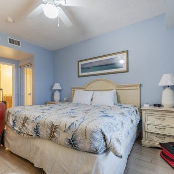 A cozy hotel room with a king-sized bed, blue walls, and bedside tables. Luggage is placed near the bed, suggesting a recent arrival.