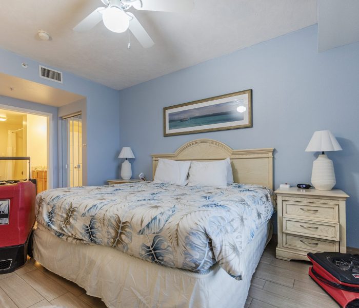A cozy hotel room with a king-sized bed, blue walls, and bedside tables. Luggage is placed near the bed, suggesting a recent arrival.