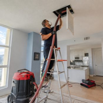 Technician on ladder cleaning air duct in Florida home