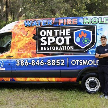A brightly colored van with advertising for water, fire, and mold restoration services, alongside a person standing next to it.